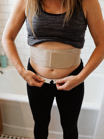 Woman adjusting a velcro postpartum belt that has ridden up her waist